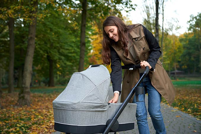 A mother is looking at her child in a bassinet stroller.