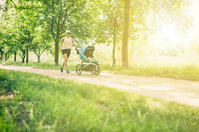A mother is jogging with her kid in the stroller.
